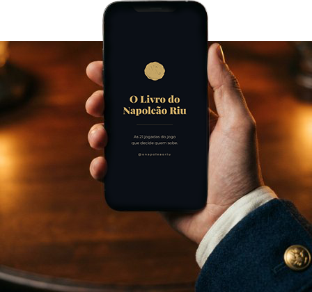 A mão do Napoleão Riu segurando o celular com a capa do livro na tela, manga de uniforme azul com botão dourado